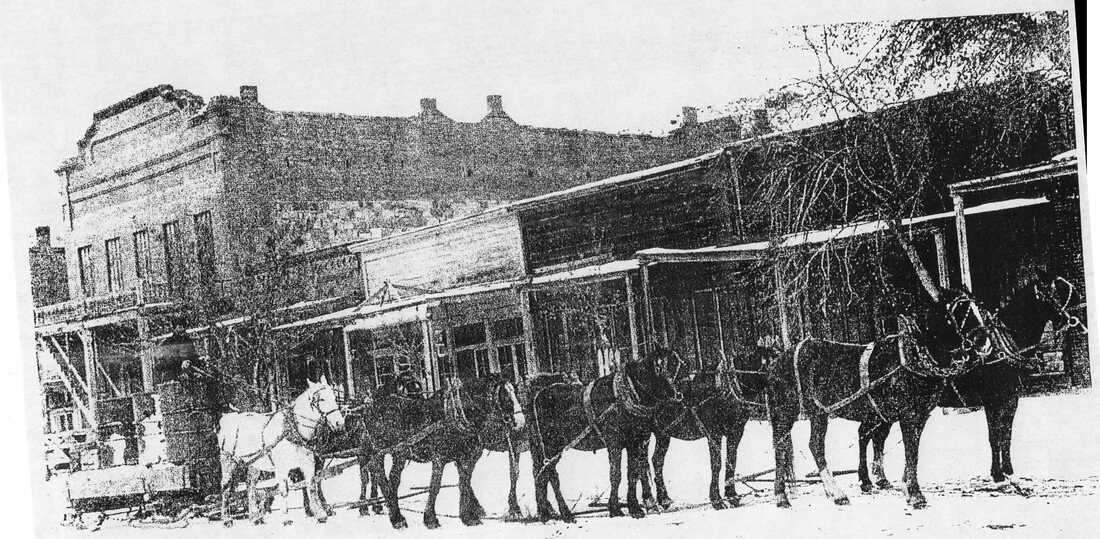Wagon team pulling sled in front of Remington Building